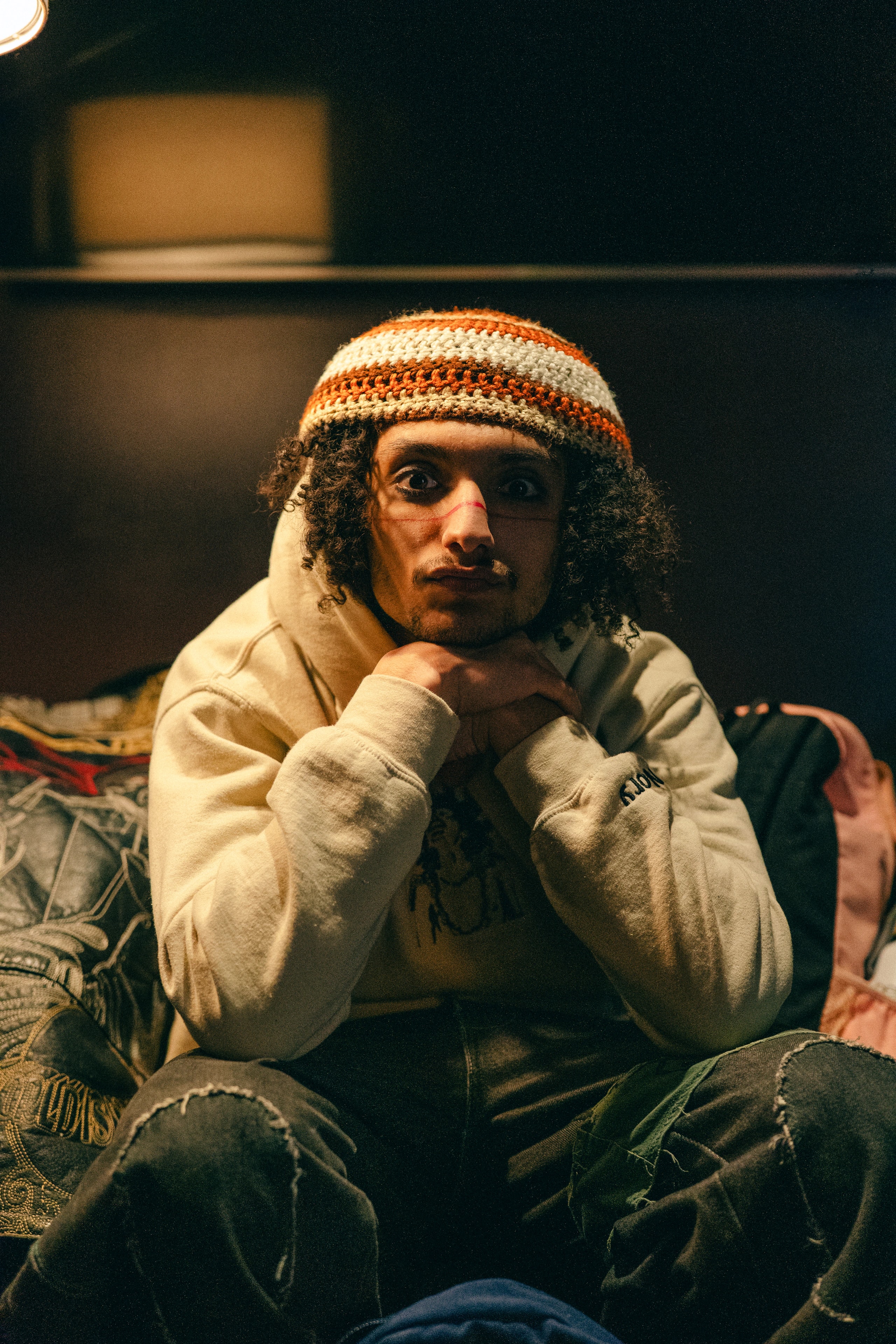 A seated person in a patterned knit cap looks toward the camera.