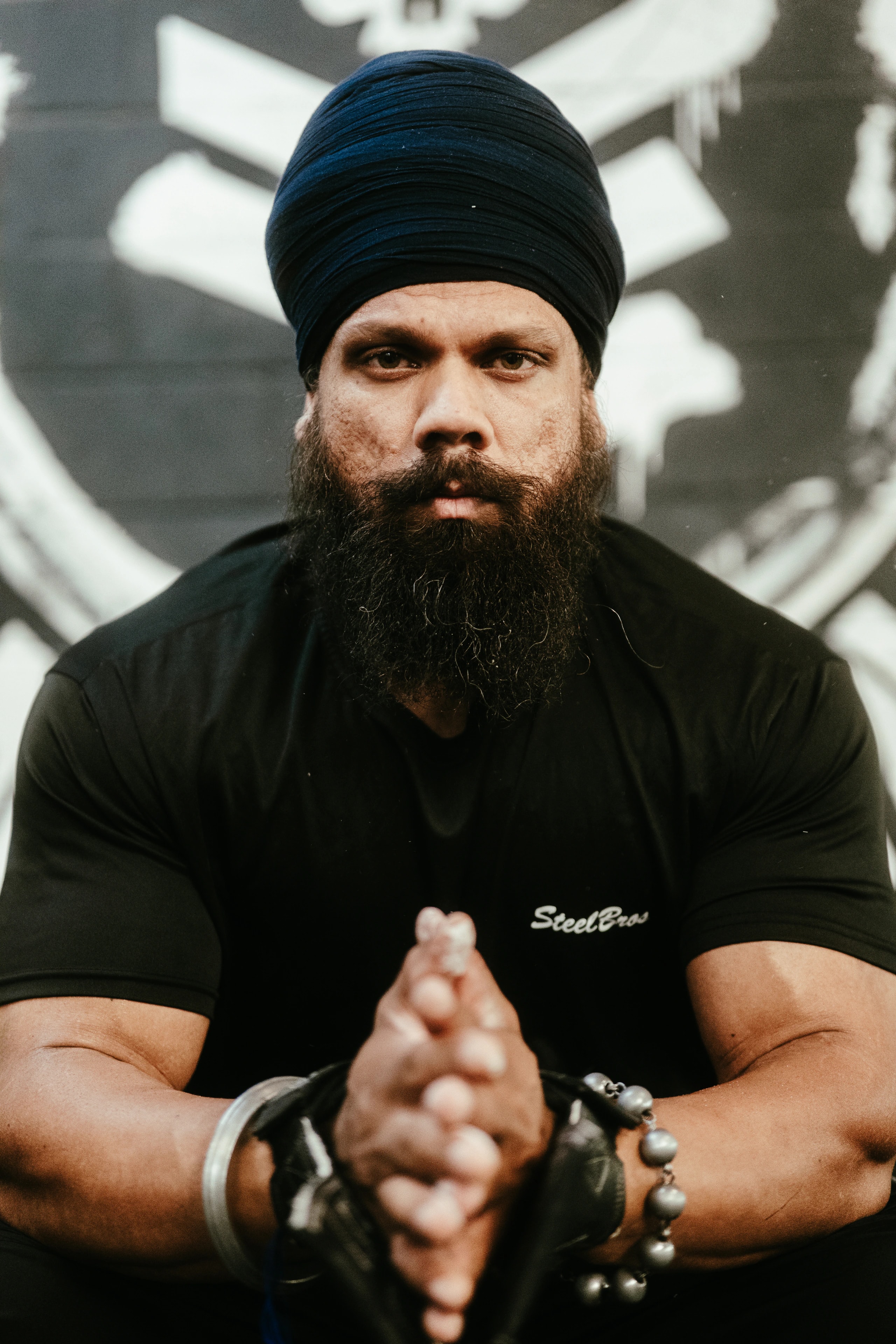 A bearded person in a black turban looks toward the camera.