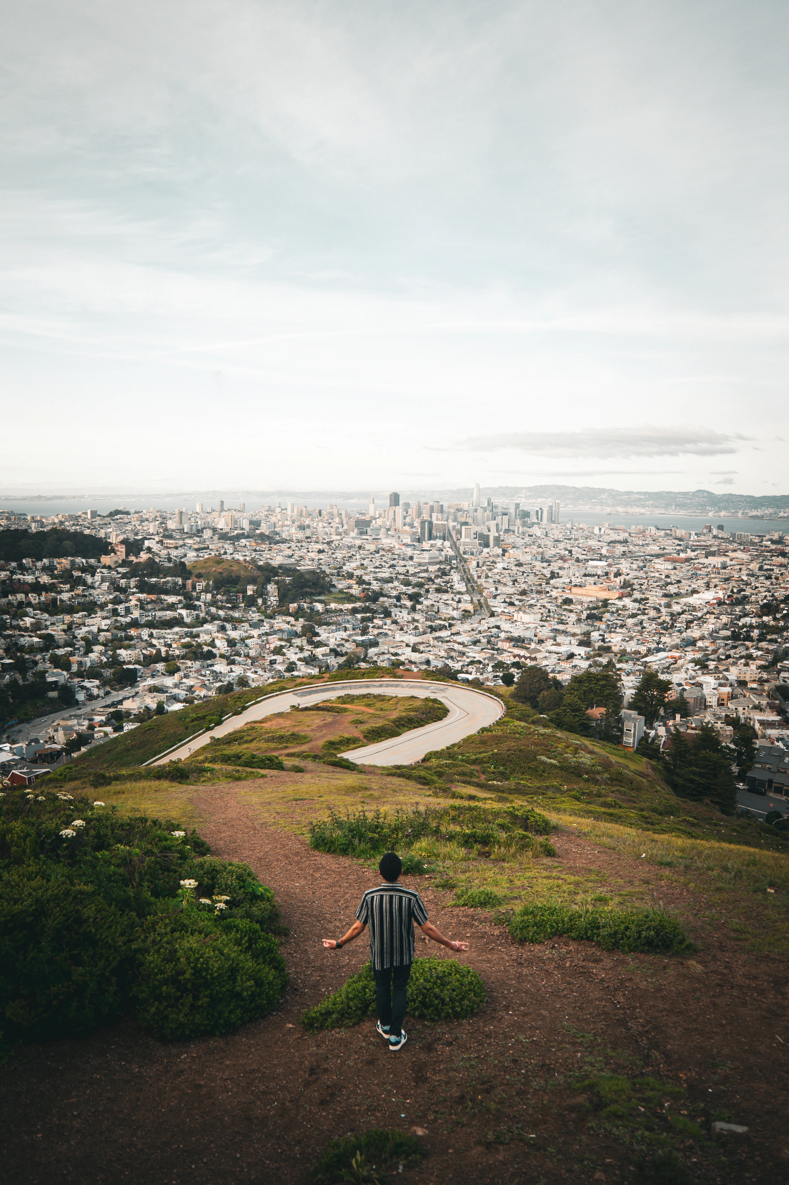 A person stands on a hillside looking toward a city below.
