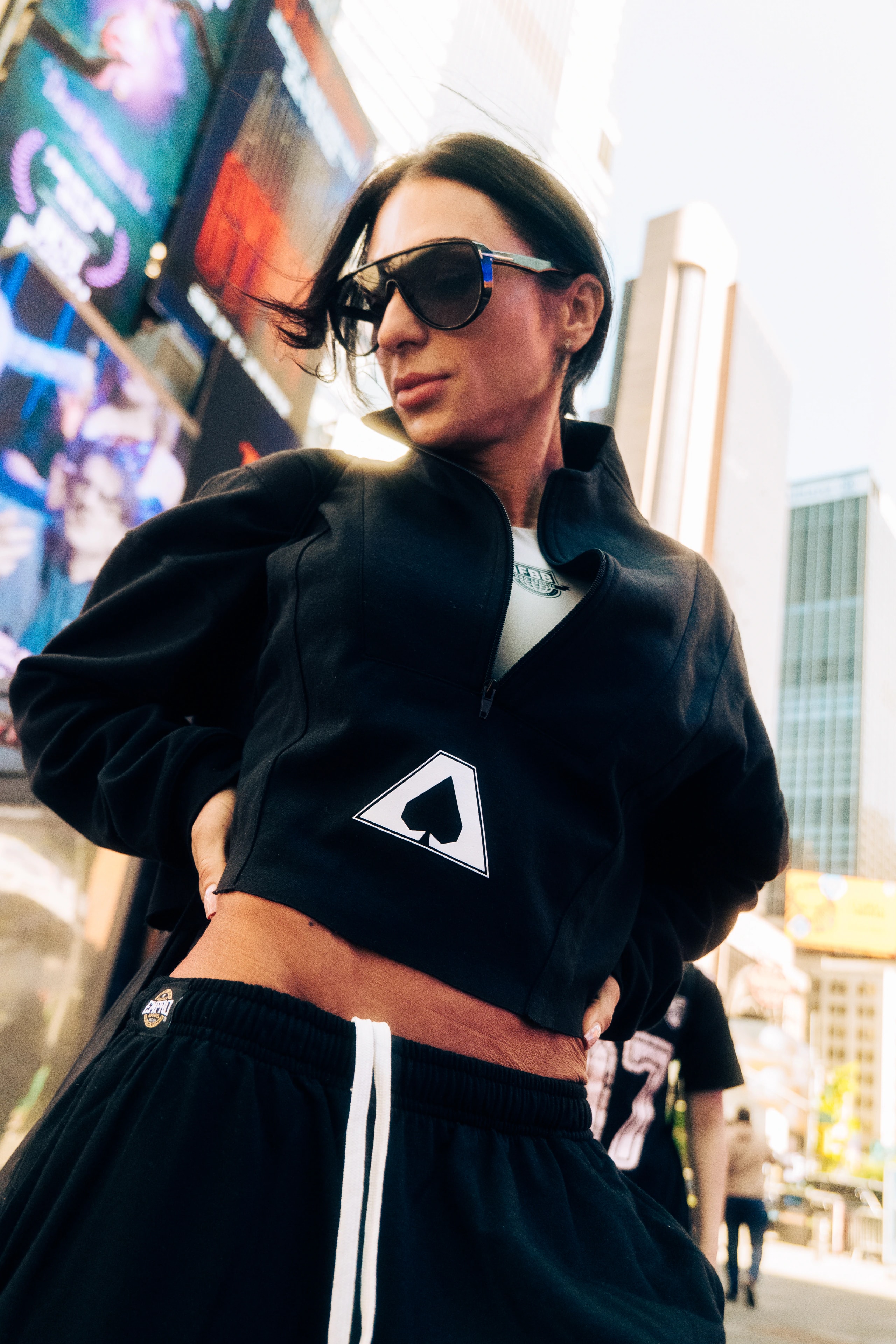 A person wearing sunglasses poses on a bright city street.
