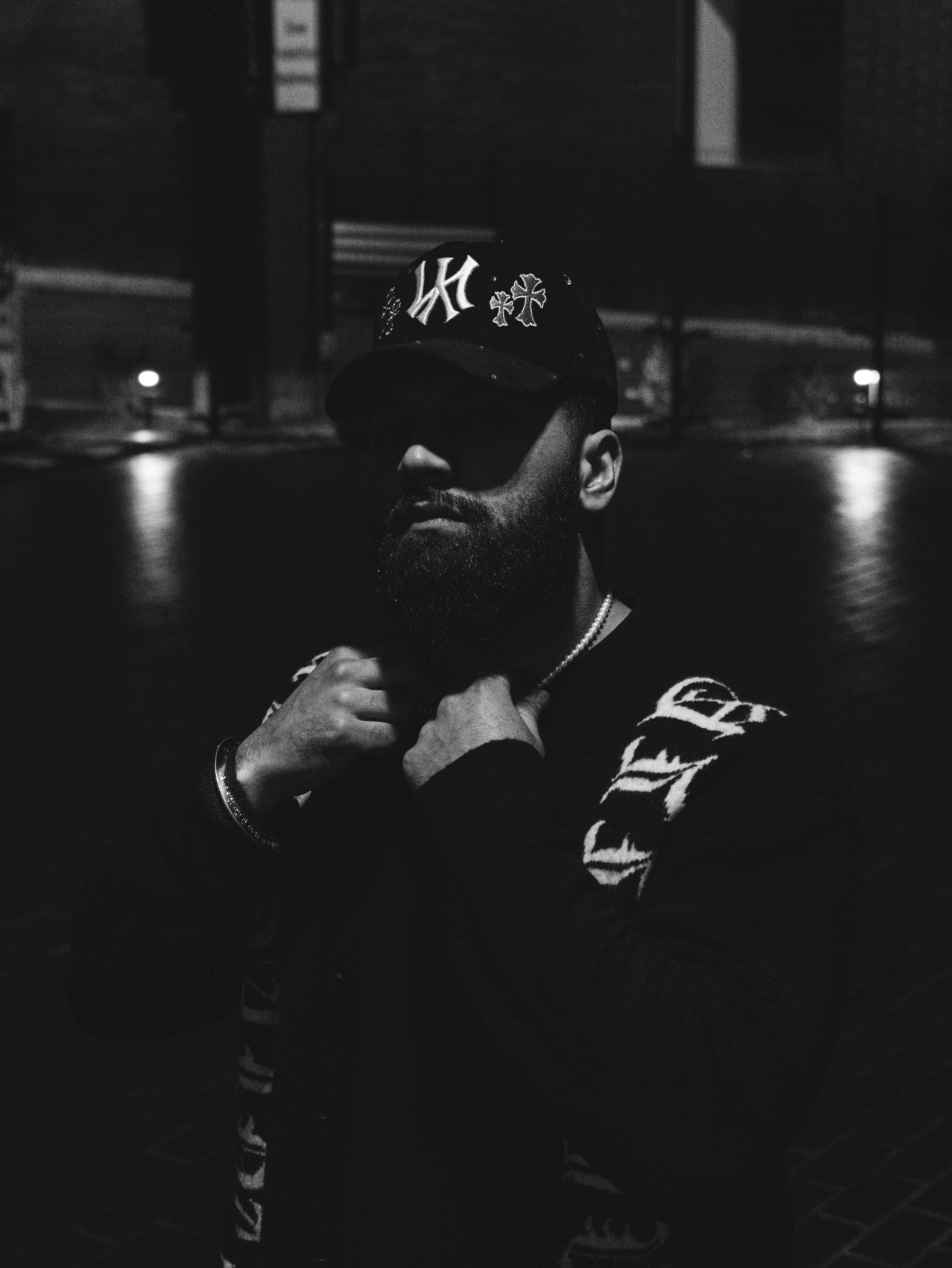 A black-and-white portrait of a bearded person wearing a cap at night.