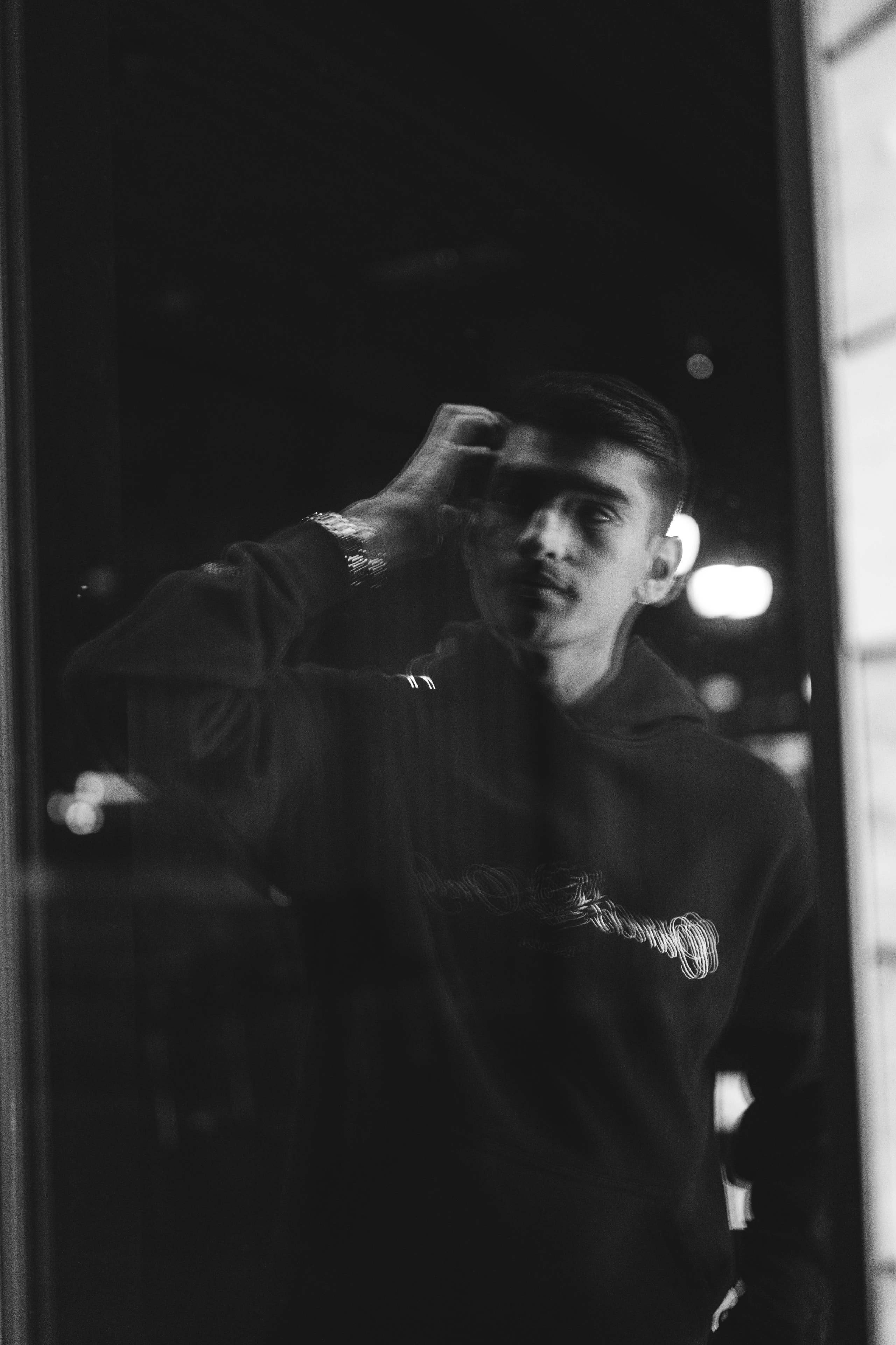 A black-and-white reflection portrait of a person touching their temple.